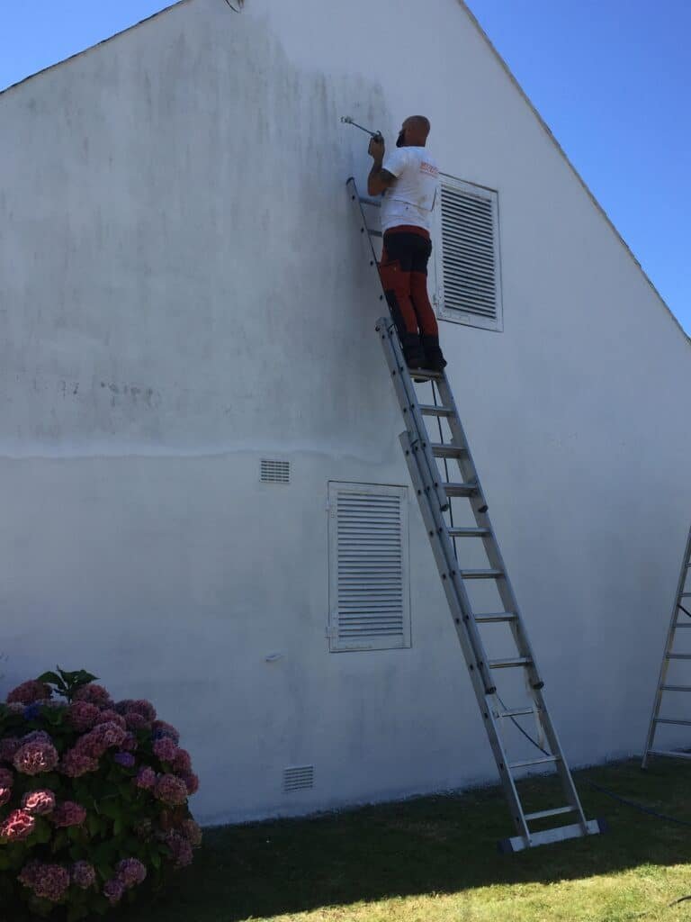 Un homme peint un mur extérieur en utilisant une échelle.