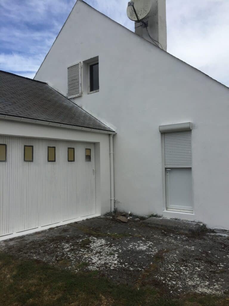 Vue de la façade blanche d'une maison avec un garage attenant.