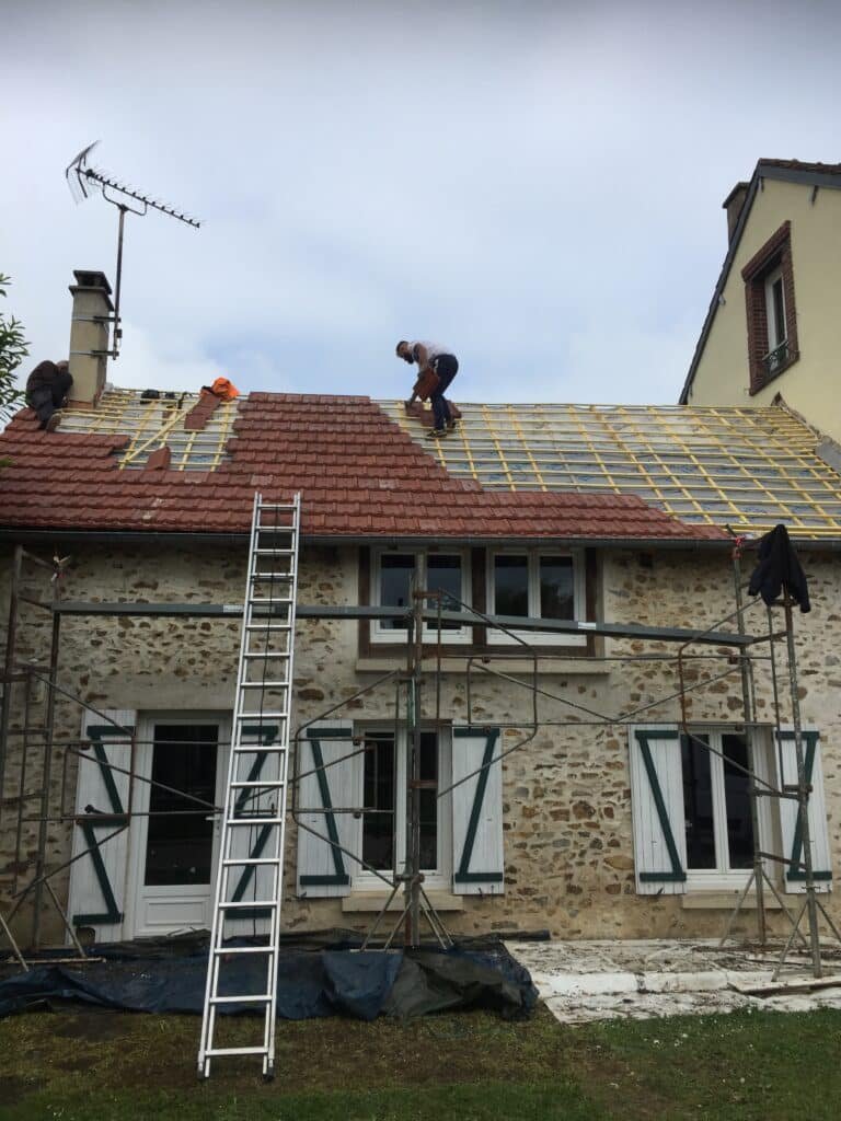 Travailleurs rénovant le toit d'une maison en pierre avec des échafaudages installés.