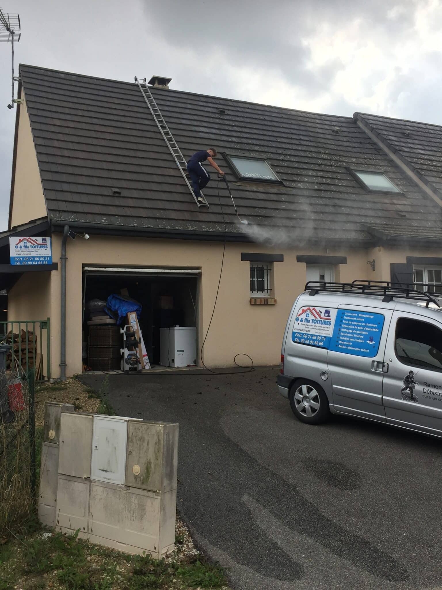 Un homme nettoie un toit en utilisant une lance à haute pression, avec une échelle appuyée sur le toit.