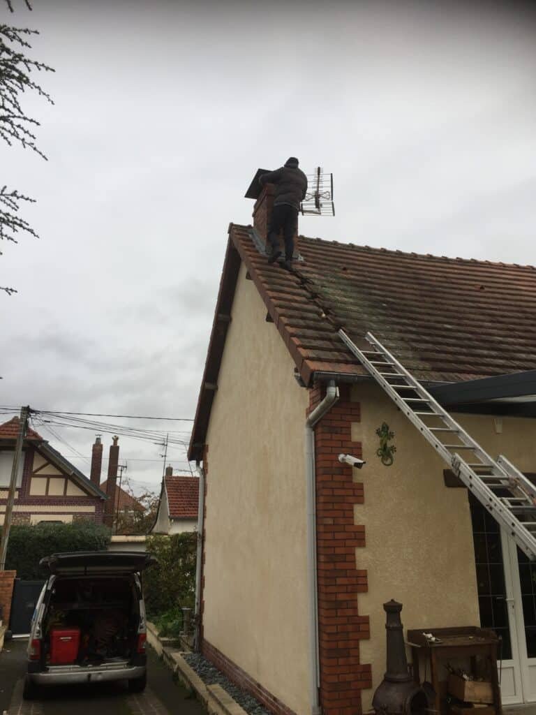 Un ouvrier effectue une réparation sur une cheminée en haut d'un toit.