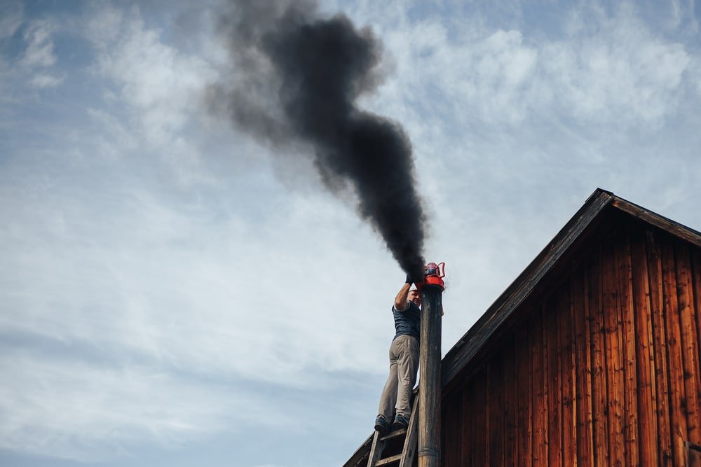 Ouvrier vérifiant une cheminée avec de la fumée noire qui s'en échappe.